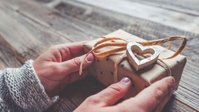 A woman's hands are holding a wrapped gift box on a wooden table.