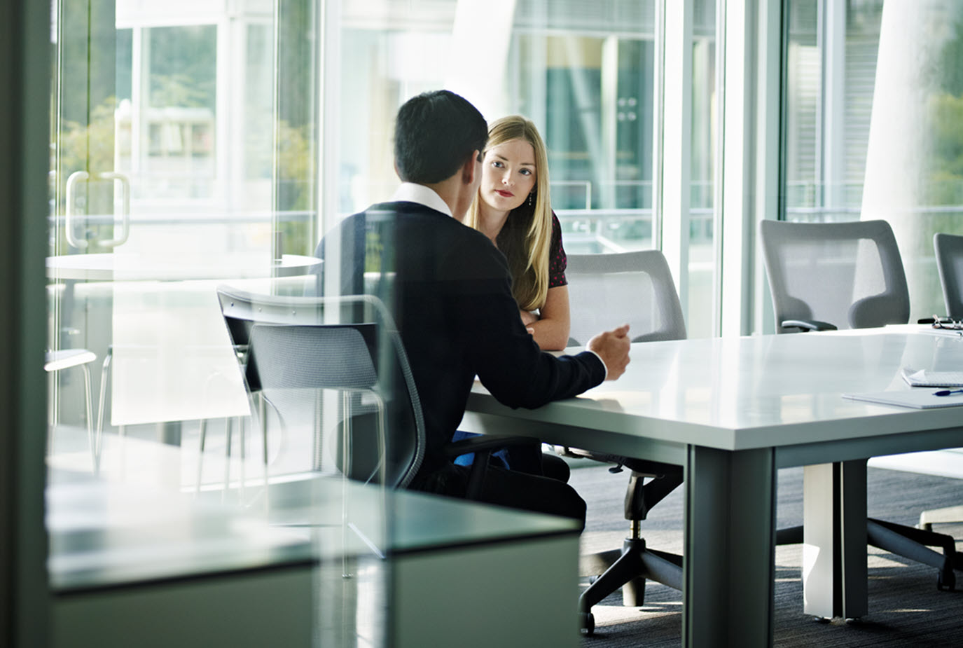 Two business people sitting at a table talk to each other.