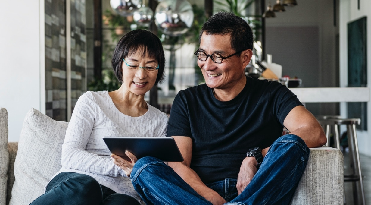 Two people sit on a couch looking at a tablet. 