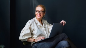 A woman smiles while working on a laptop.