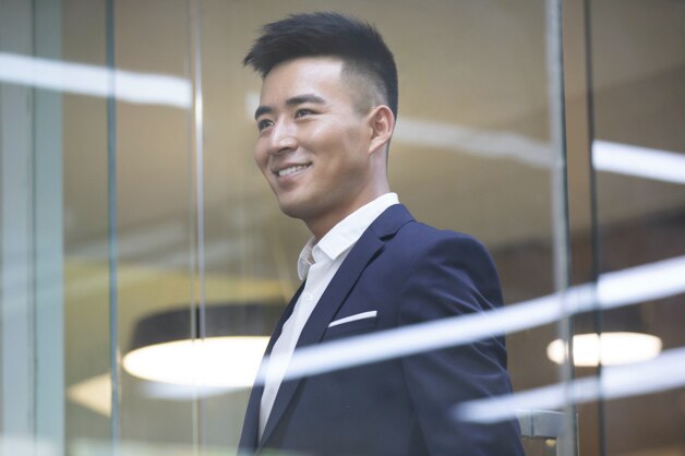 A businessperson smiles as he looks through the window of an office building.