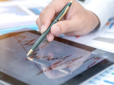 A closeup of an investment advisor's hand using a pen to point to a graph on a tablet computer