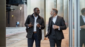 Two people in suits walk down the street together.