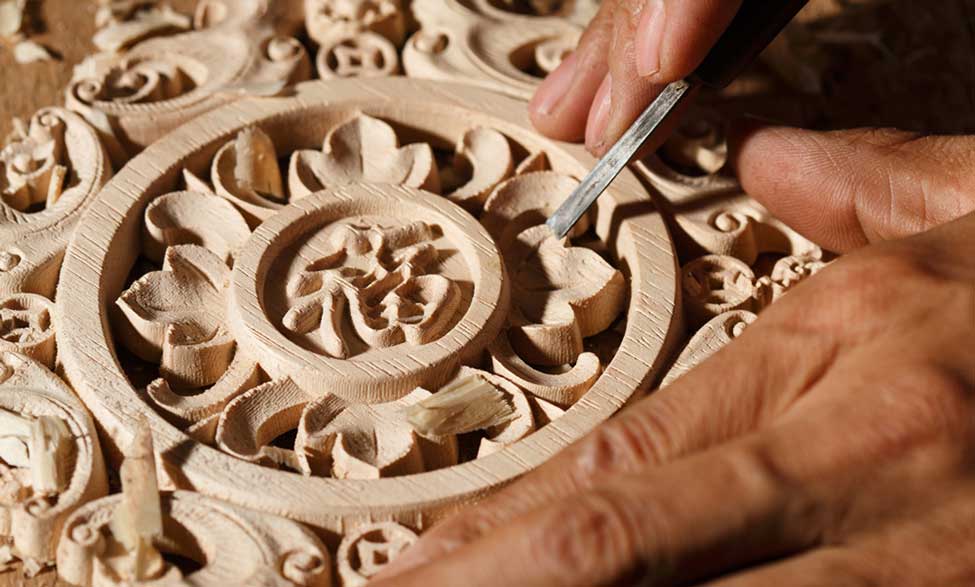 A close-up of hands carving wood in a detailed pattern