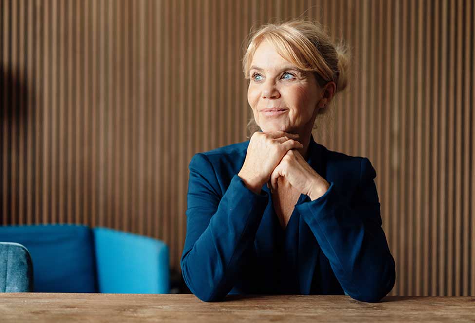 A professional sits at a desk, smiling and looking off into the distance
