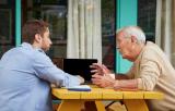 Older man and younger man talking at a picnic table with a laptop.
